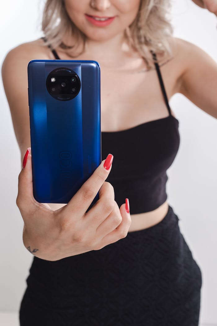 digital A woman with red nails holds a blue smartphone, ready to take a selfie.